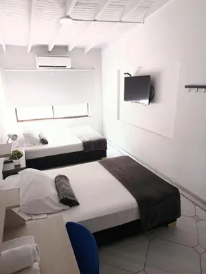 two beds in a white room with a tv at Hotel la Carpita in El Poblado