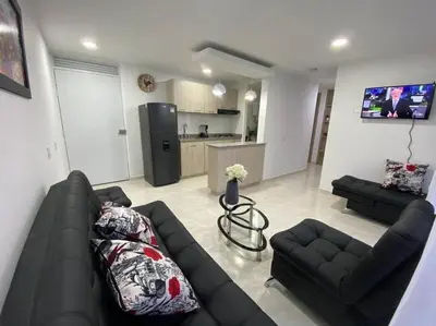 a living room with a black couch and a kitchen at Acogedor Apartamento Como en casa in Manizales