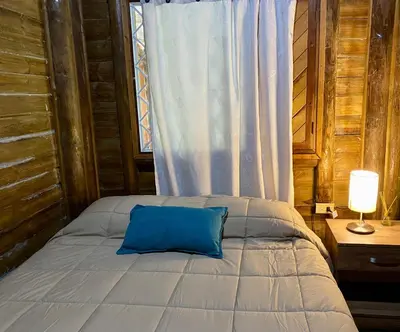 a bed with a blue pillow in a room with a window at Cabaña rústica la Pradera in Guatapé
