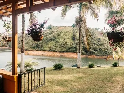 a porch with a view of a river and palm trees at Volare Guatapé isla de descanso y retiro in Guatapé