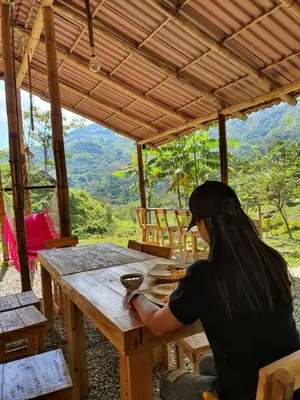 a woman sitting at a wooden table with a view at Cabañas la tierra prometida in Cisneros