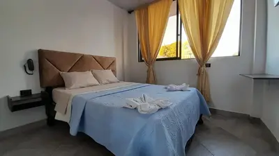 a bedroom with a bed with a blue blanket and windows at Katara Boutique Hotel in Mariquita