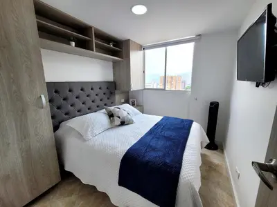 a bedroom with a bed with a blue blanket and a tv at Modern High-Rise 2/2 Apartment with City View. in Sabaneta